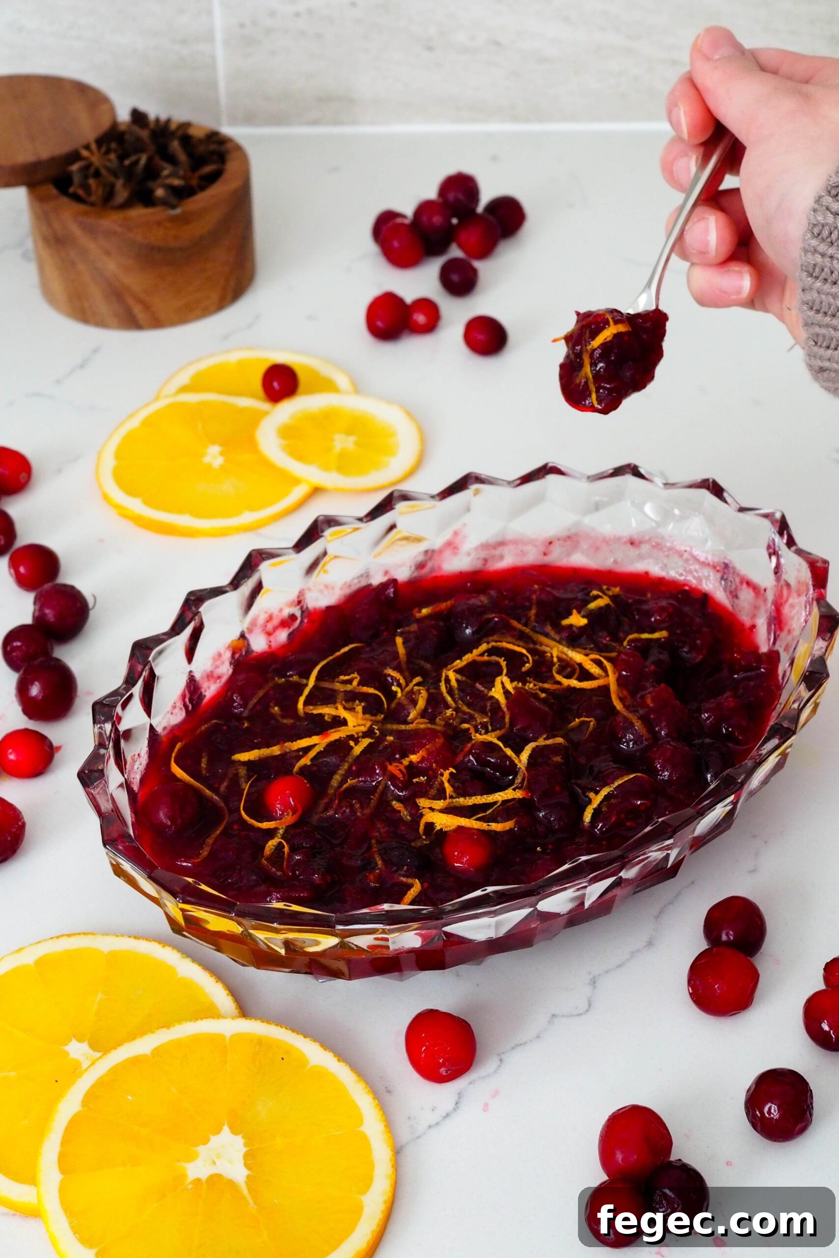 A hand scoops a small serving of cranberry sauce out of a crystal serving dish.