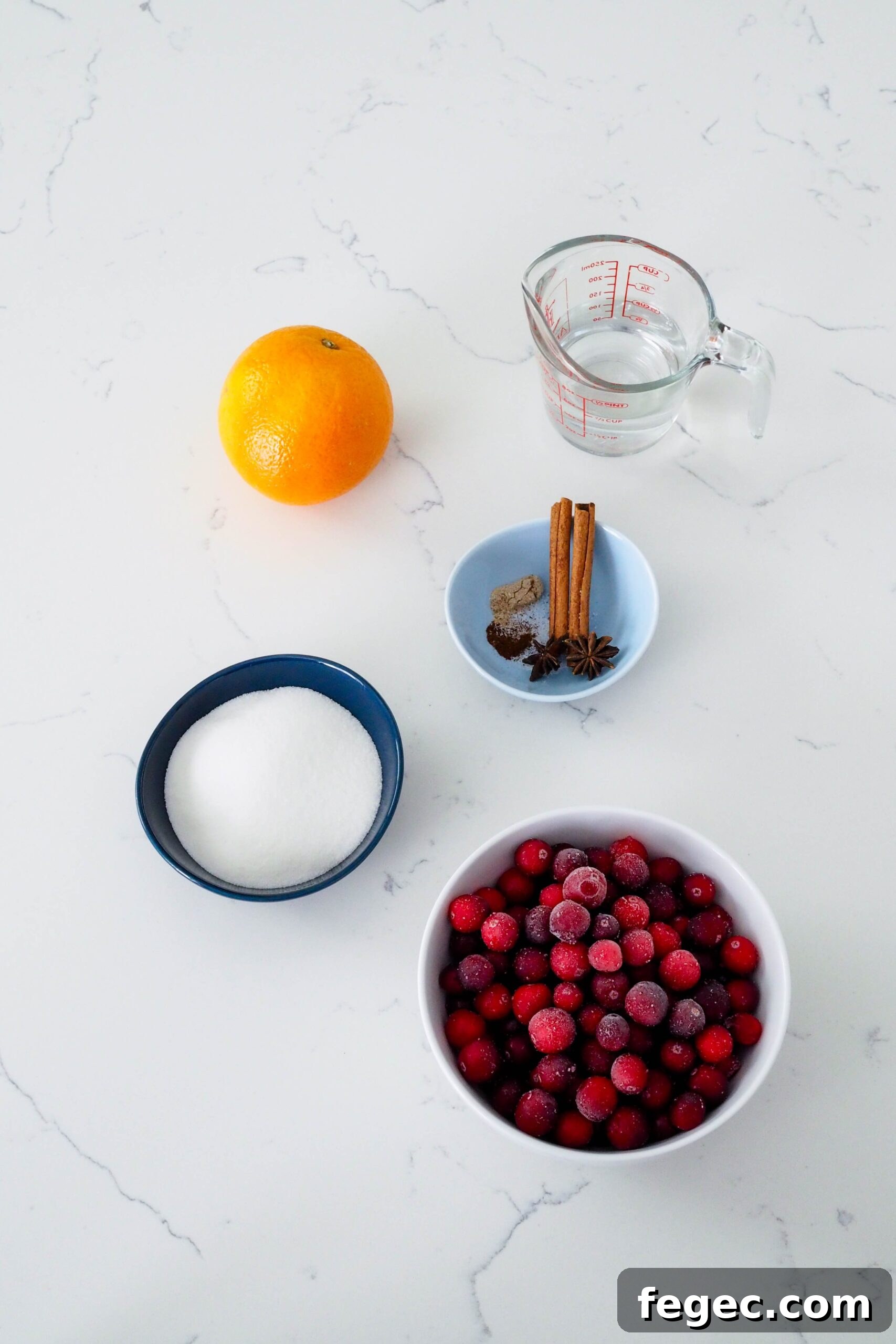 Frozen cranberries, sugar, an orange, spices, and water on a quartz counter.