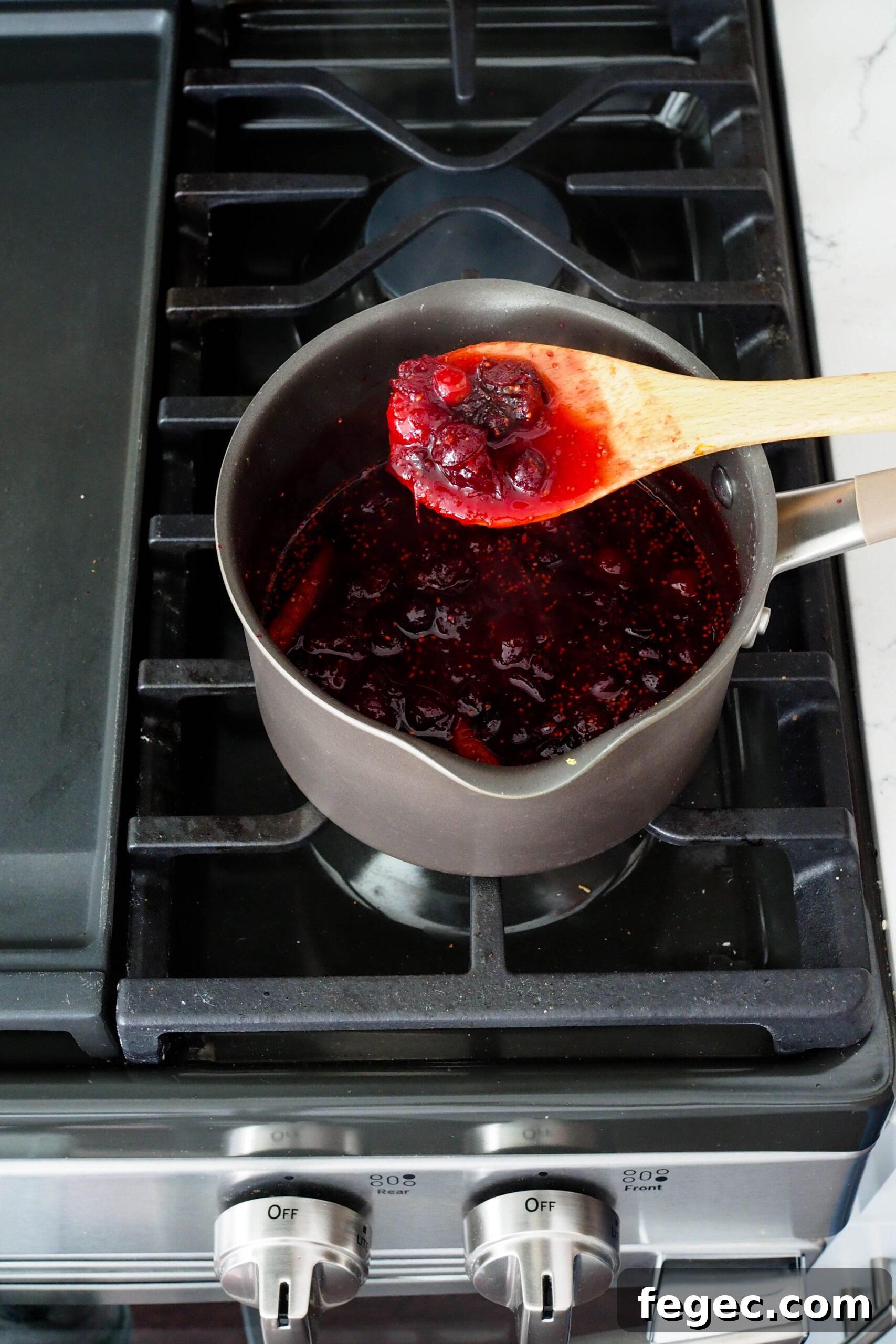A wooden spoon holds up some cranberry sauce.