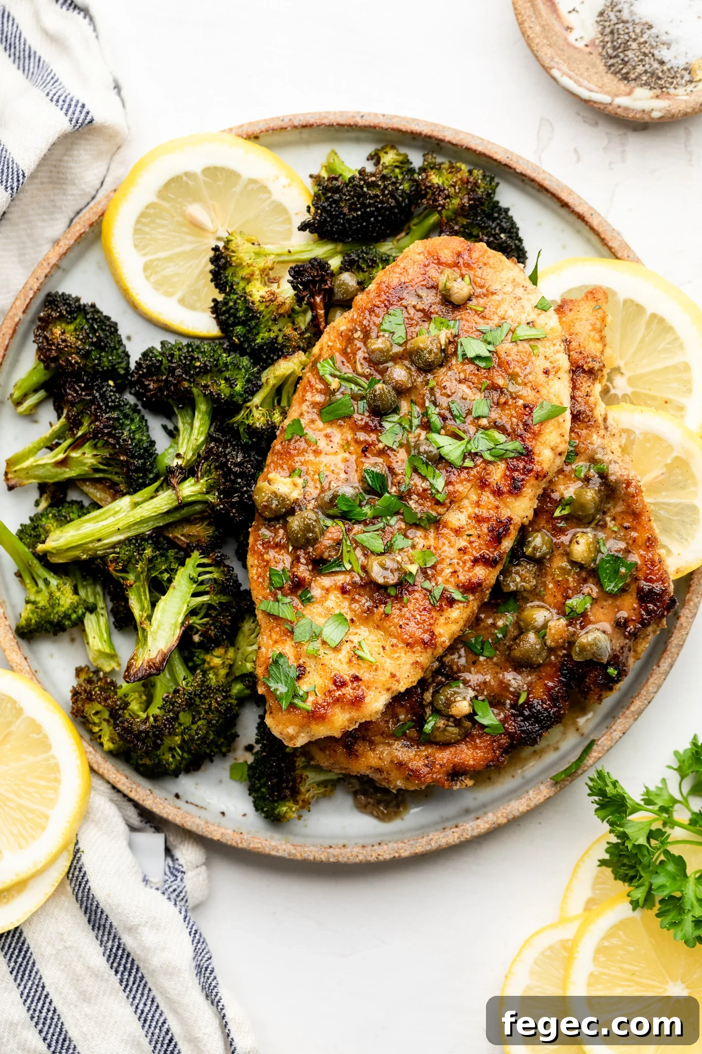 Gluten-Free Chicken Piccata with Lemon Caper Sauce 6 A tan and white plate with roasted broccoli, gluten free chicken piccata, and lemon slices