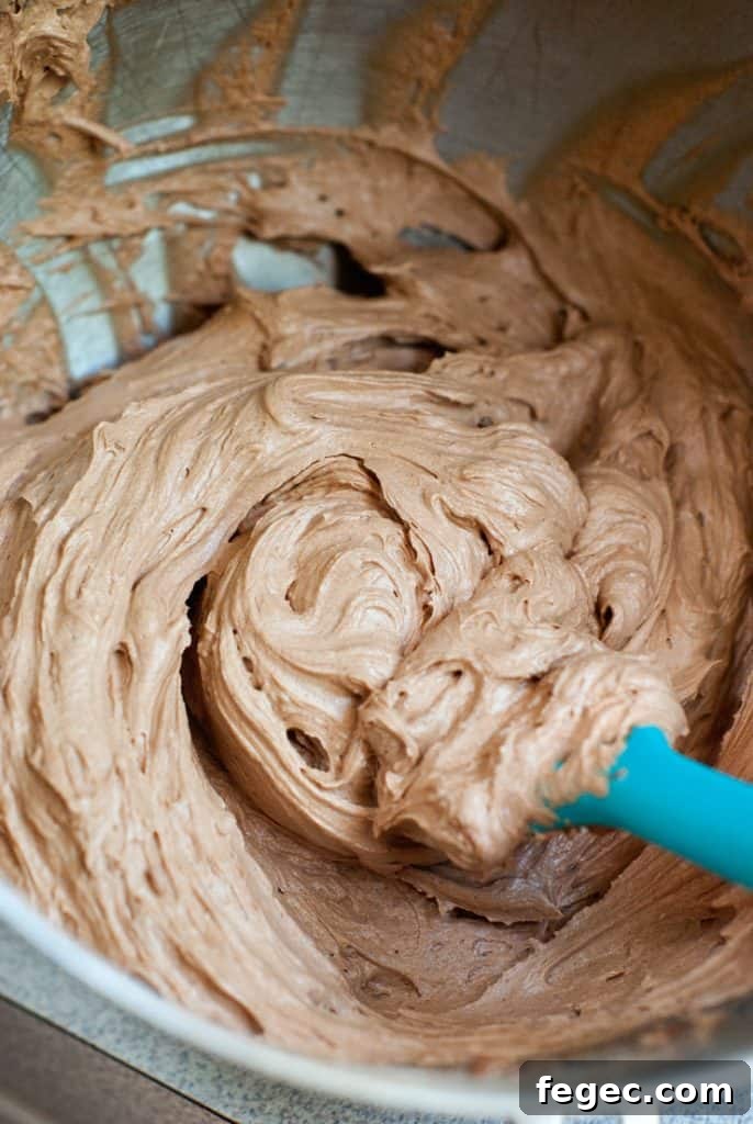 Mixing simple Chocolate Frosting in a mixing bowl with a blue spatula.