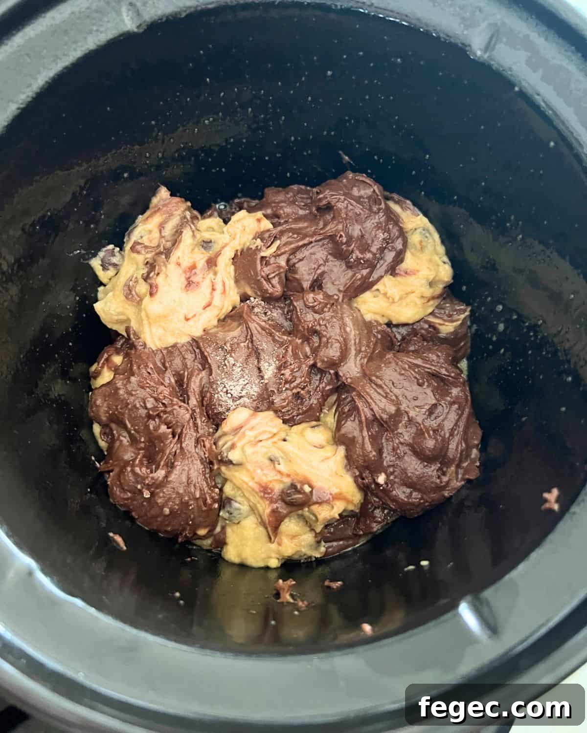 Alternating brownie batter and cookie dough batter together in a crock pot. 