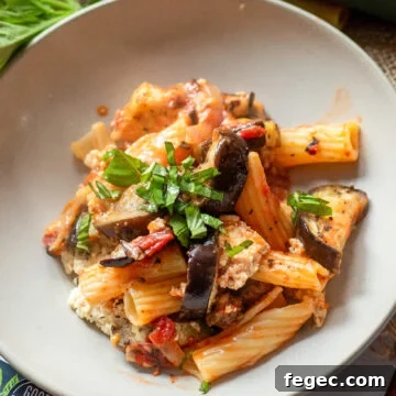 close up view of a white plate with vegan eggplant pasta made with roasted pasta, tomato sauce, and vegan cheese.