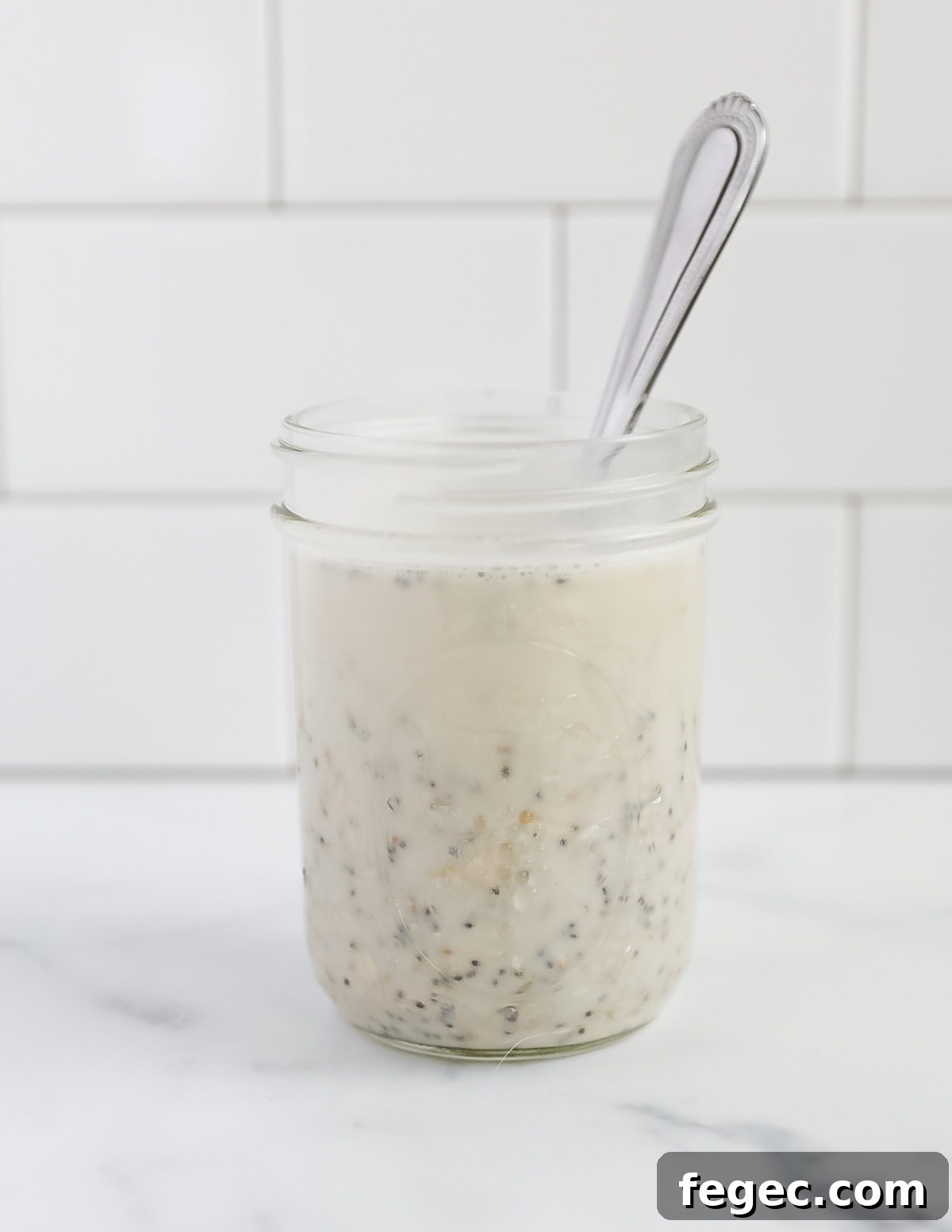 Creamy Chia Seed Overnight Oats Recipe for Busy Mornings 4 A mason jar with unmixed oatmeal and plant based milk. There is a spoon in the jar
