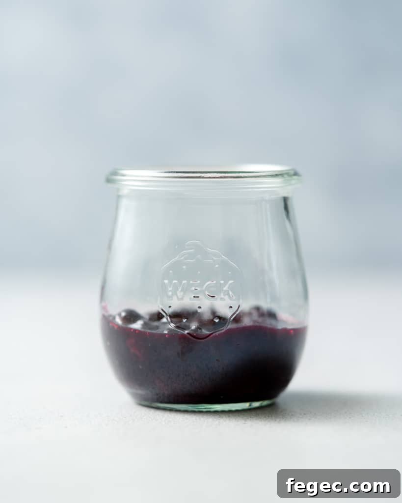 Adding blueberry sauce to a glass jar.