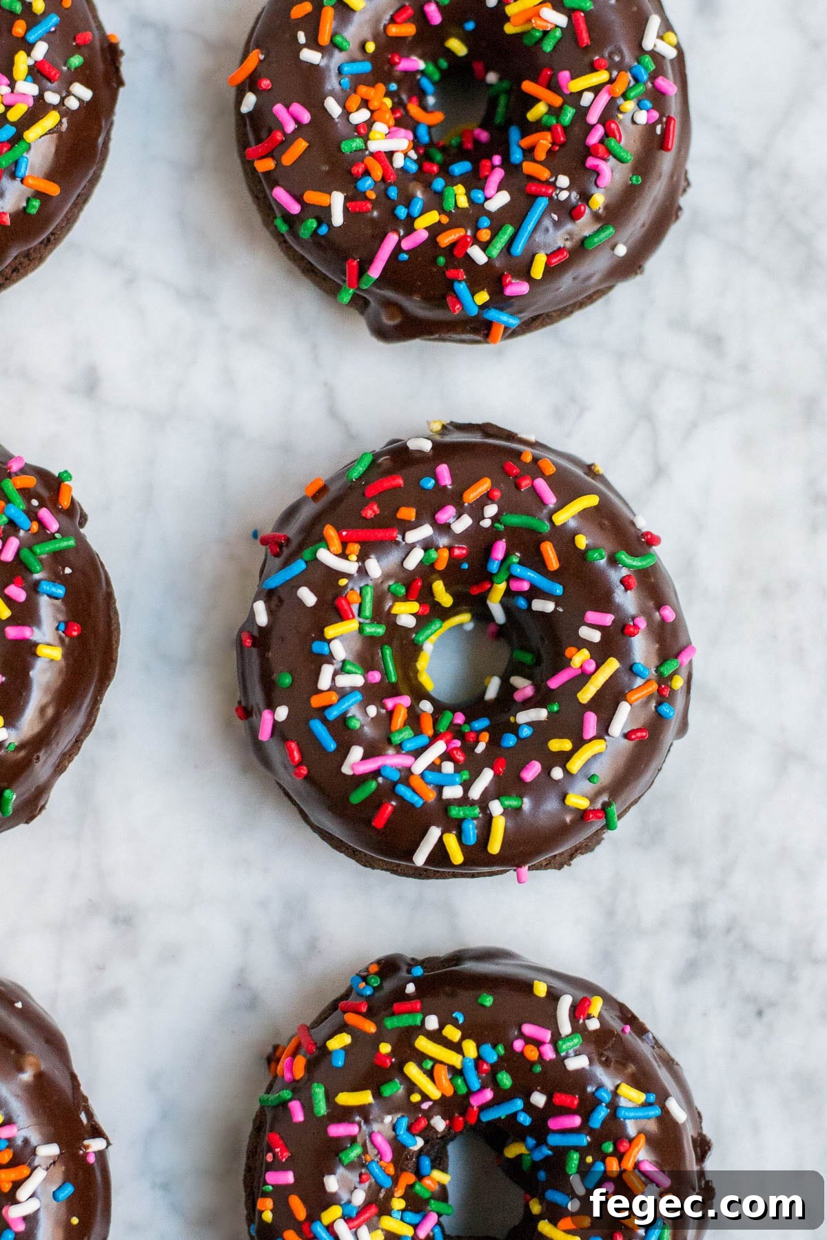 An aerial view of chocolate donuts with sprinkles on a marble table.