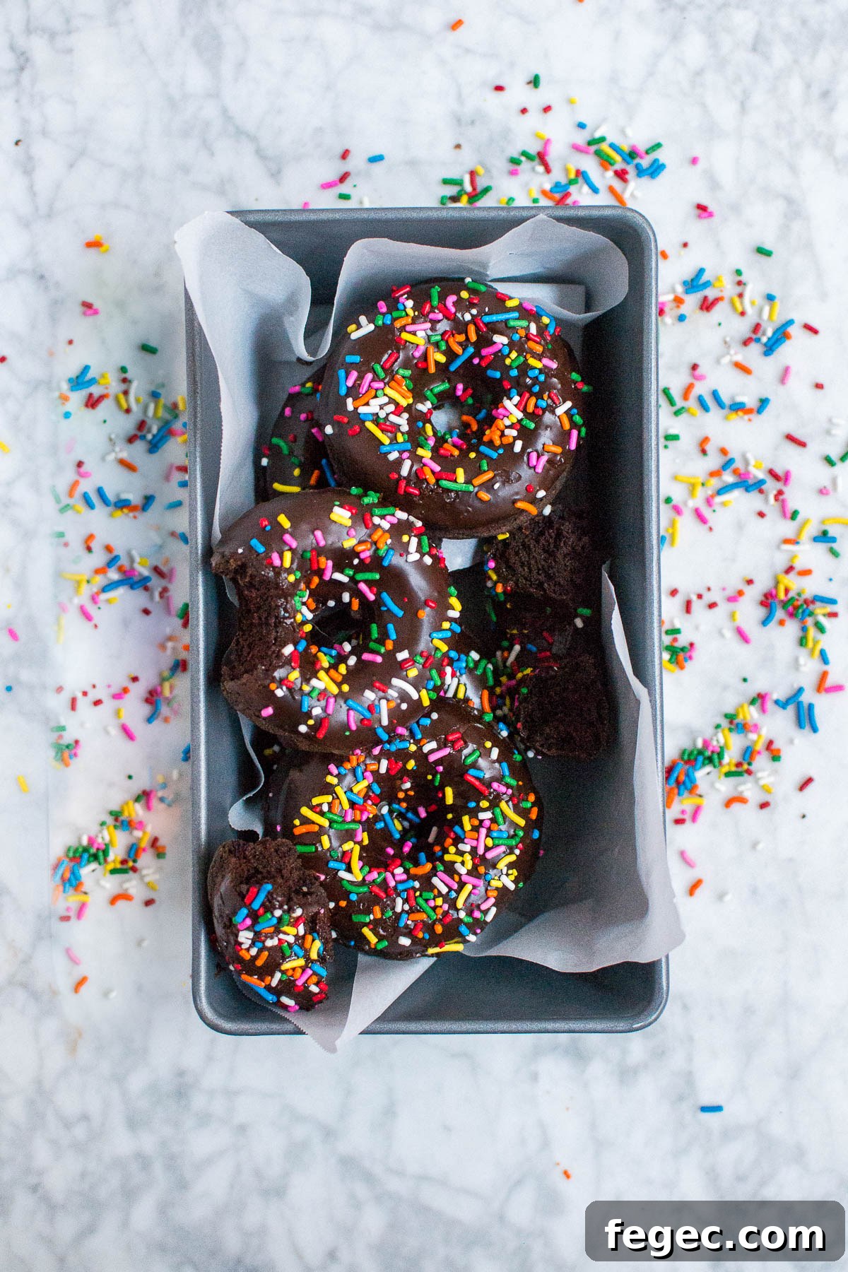 An aerial view of gluten-free vegan chocolate donuts with sprinkles in a metal loaf pan
