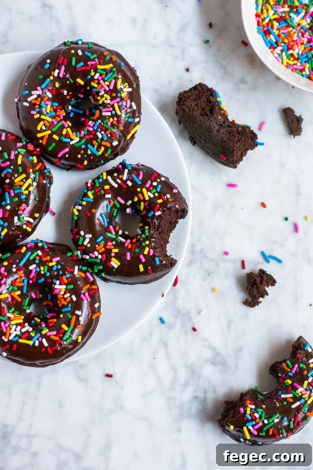 Aerial view of a plate with donuts and pieces of donuts on a marble table and a small bowl with sprinkles in the upper right hand corner.