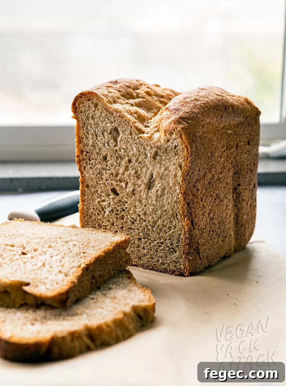 two slices of wheat bread next to the loaf and bread knife