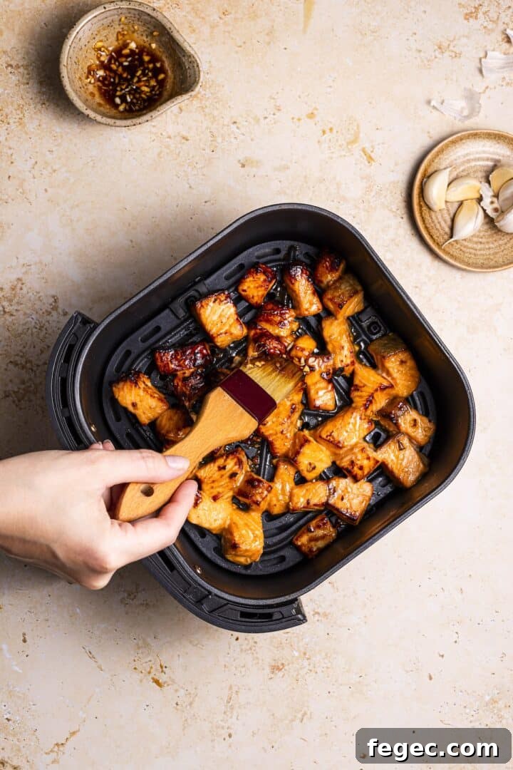 Salmon bites being brushed with marinade in an air fryer basket.
