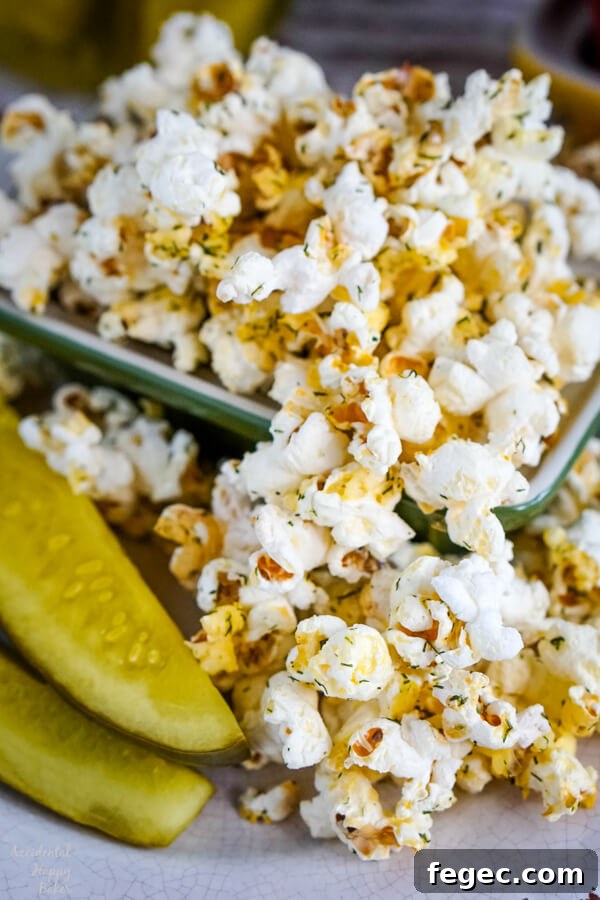 A bowl of dill pickle popcorn next to two dill pickle spears.