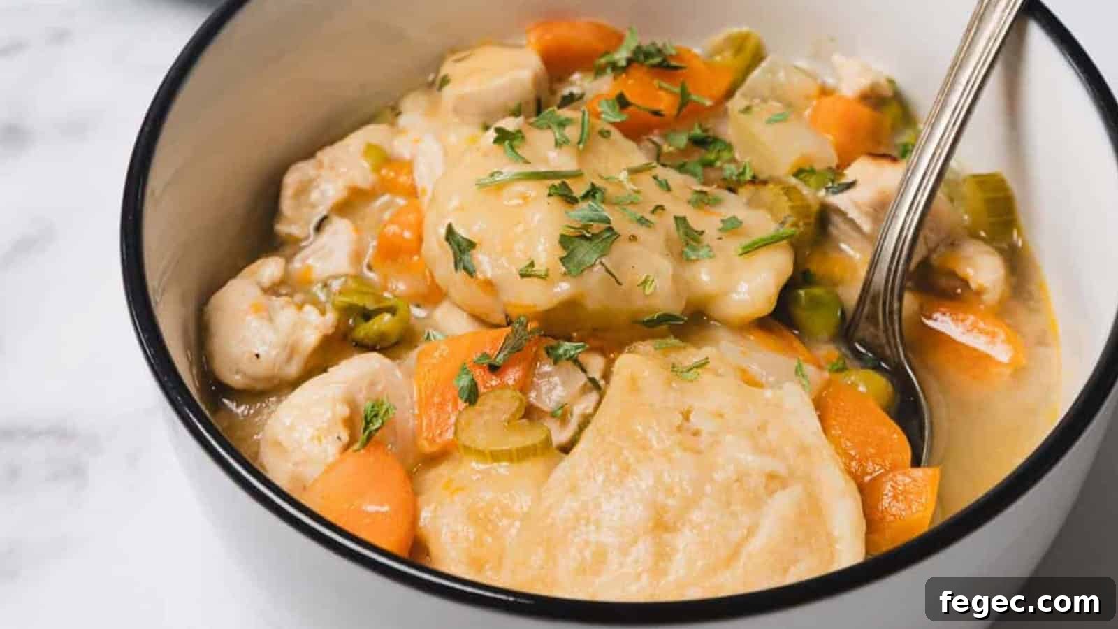 15 Flavor-Packed Skillet Recipes for Quick Cleanup 13 A bowl of chicken and dumplings soup with carrots, celery, and herbs, with a spoon inside.