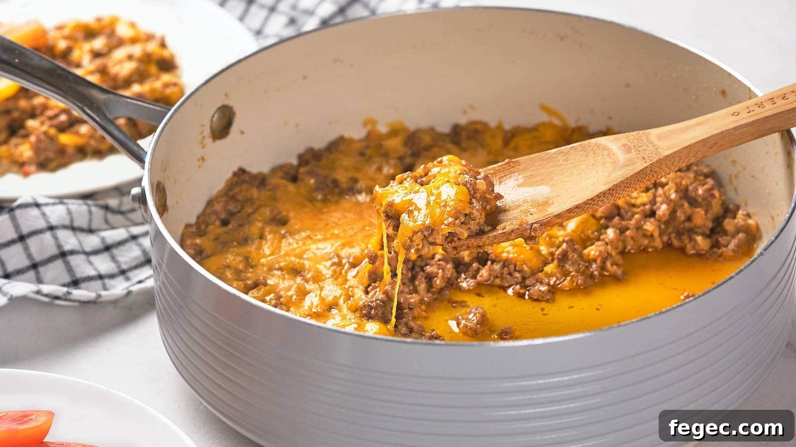 15 Flavor-Packed Skillet Recipes for Quick Cleanup 17 A wooden spoon scoops a portion of cooked ground meat with melted cheese from a pan.