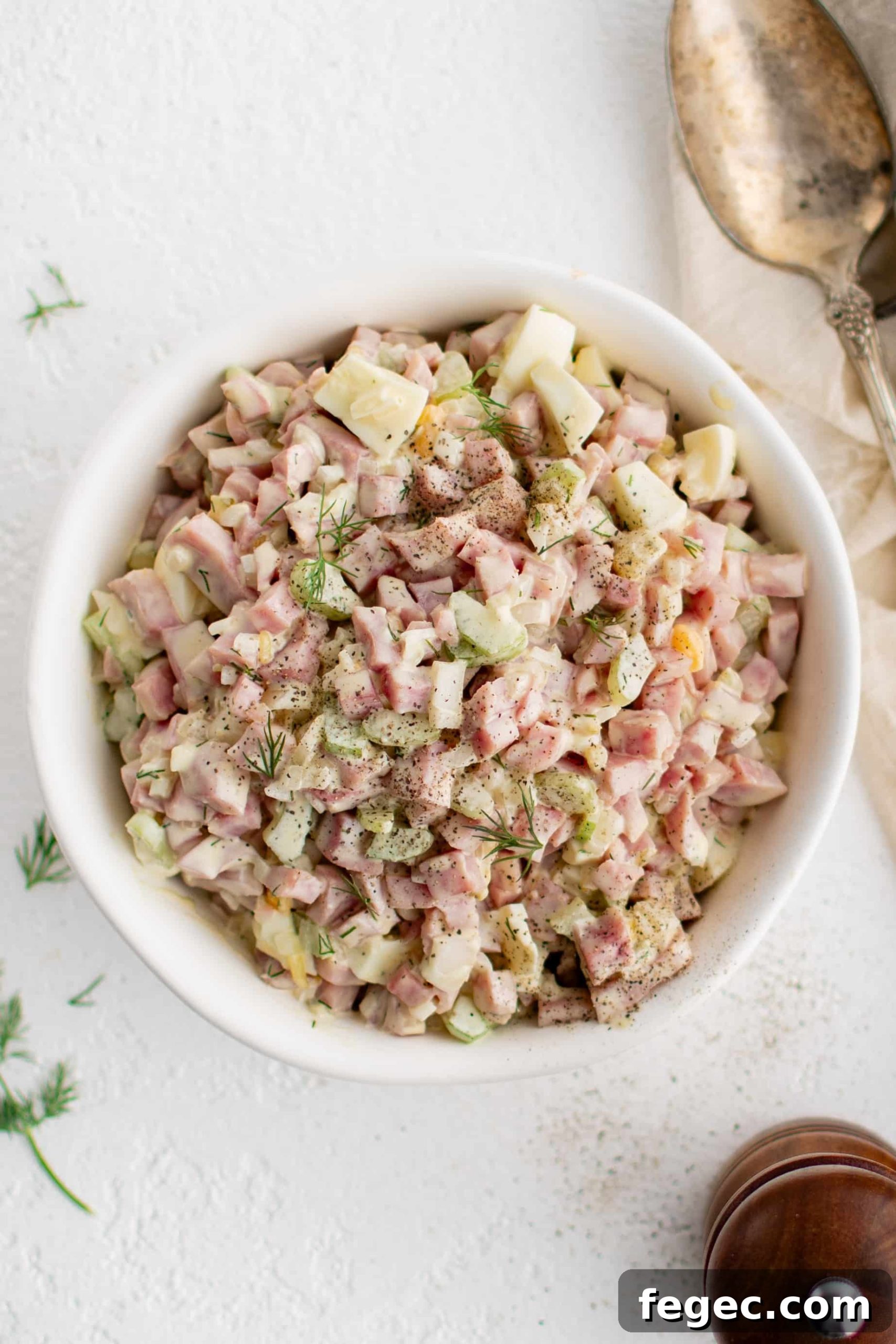 White serving bowl filled with creamy ham salad made with diced pieces of ham, celery, hard-boiled egg, and onion.