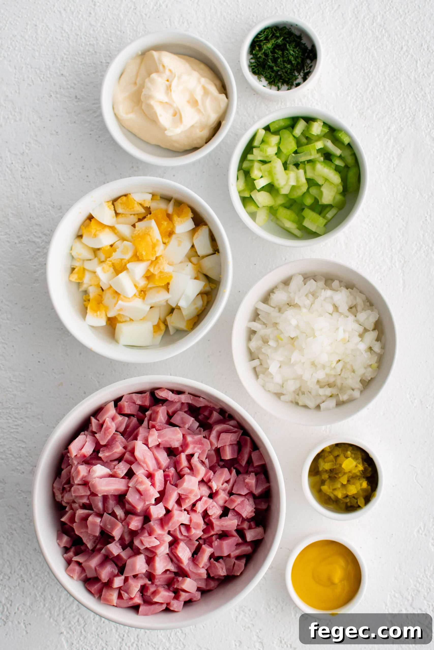 Ingredients needed to make ham salad recipe in individual measuring cups and ramekins.