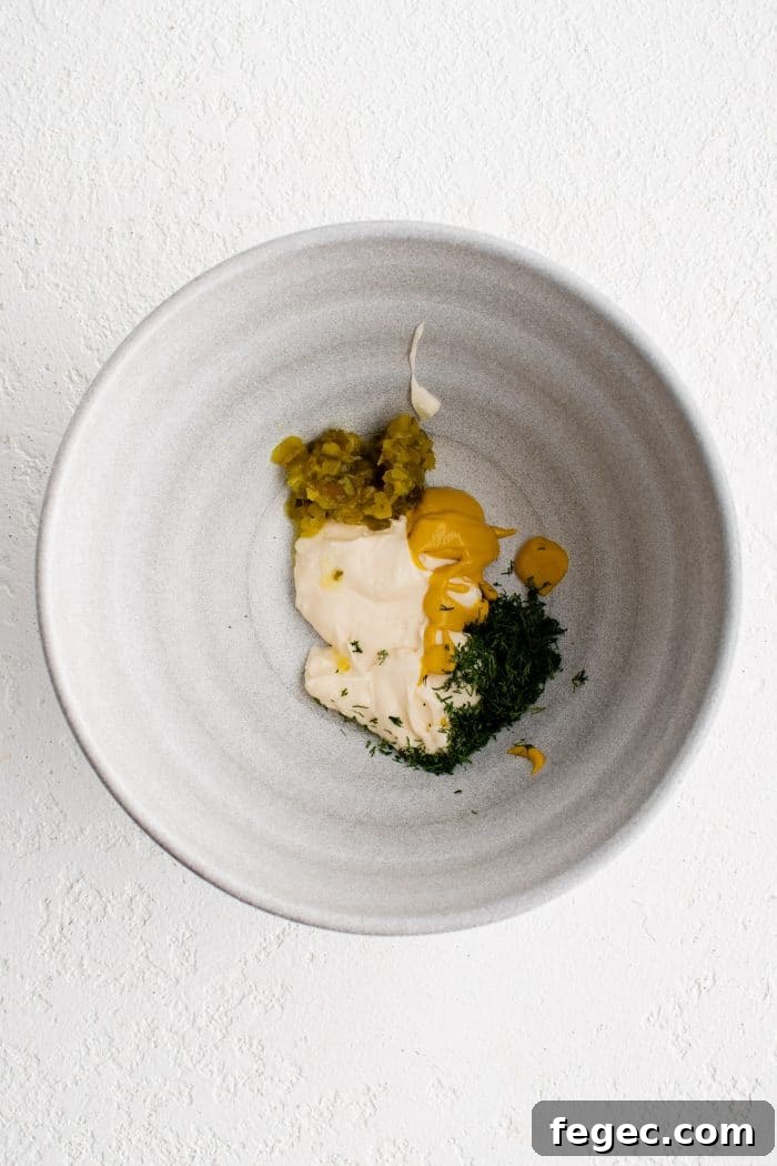 Large white mixing bowl with mayonnaise, mustard, dill pickle relish, and fresh dill.