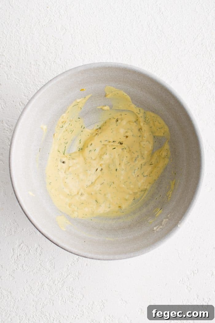 Large white mixing bowl filled with creamy mayonnaise mixture for ham salad.