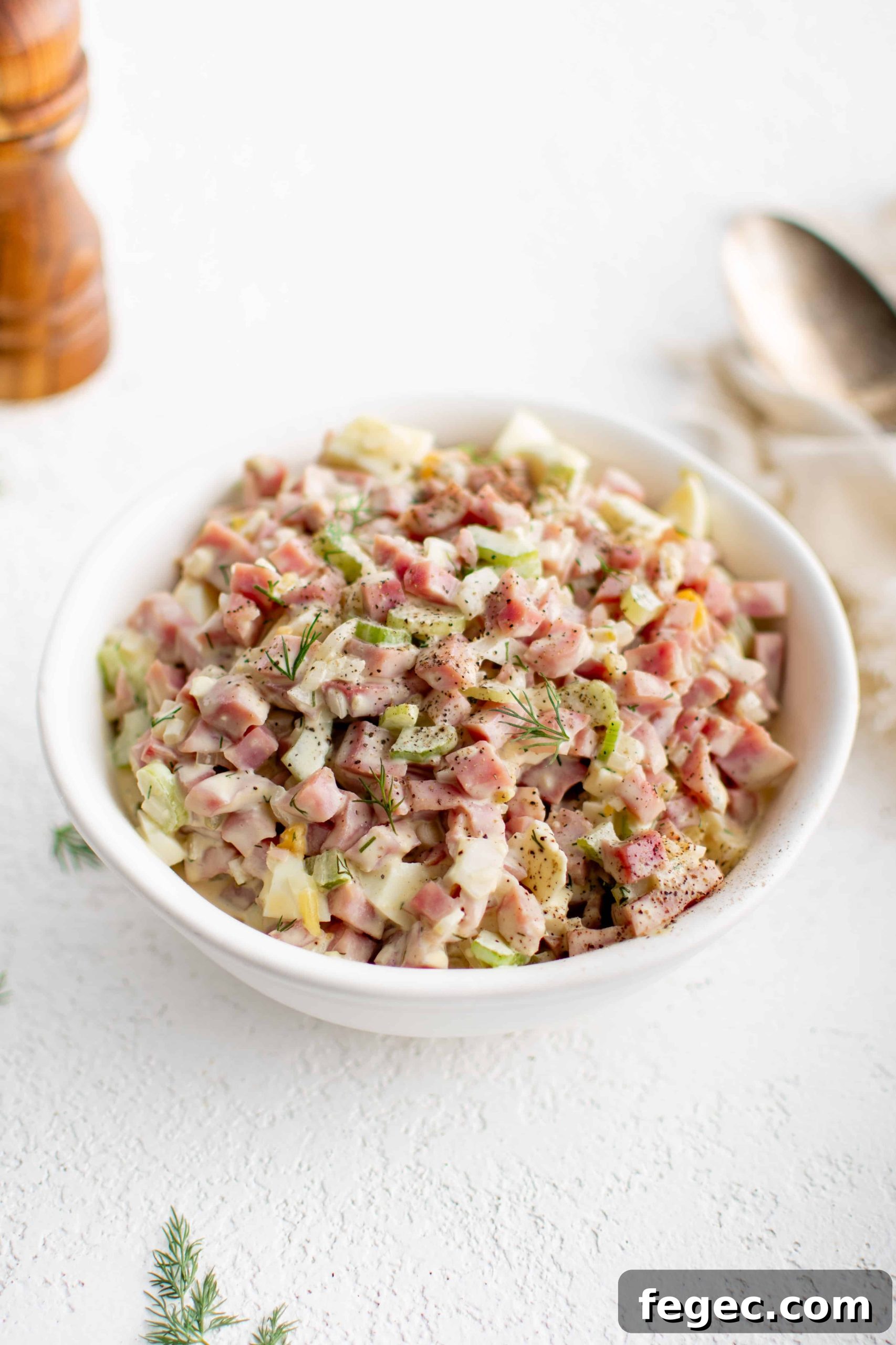 White serving bowl filled with creamy ham salad made with diced pieces of ham, celery, hard-boiled egg, and onion.
