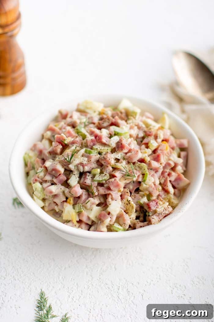 White serving bowl filled with creamy ham salad made with diced pieces of ham, celery, hard-boiled egg, and onion.
