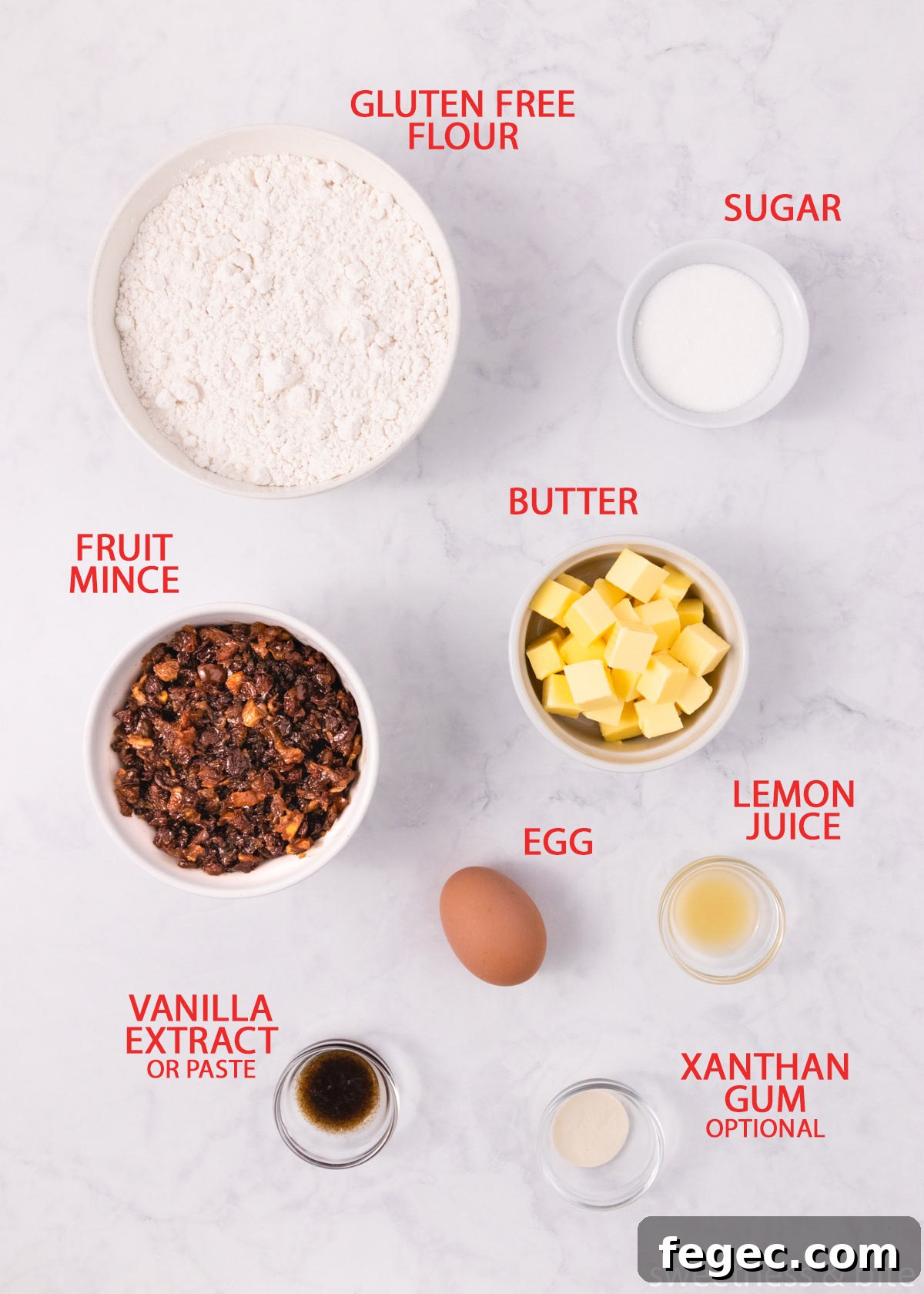The gluten free mince pie ingredients in small bowls on a grey marble background - gluten free flour, sugar, butter, lemon juice, xanthan gum, egg, vanilla and fruit mince.
