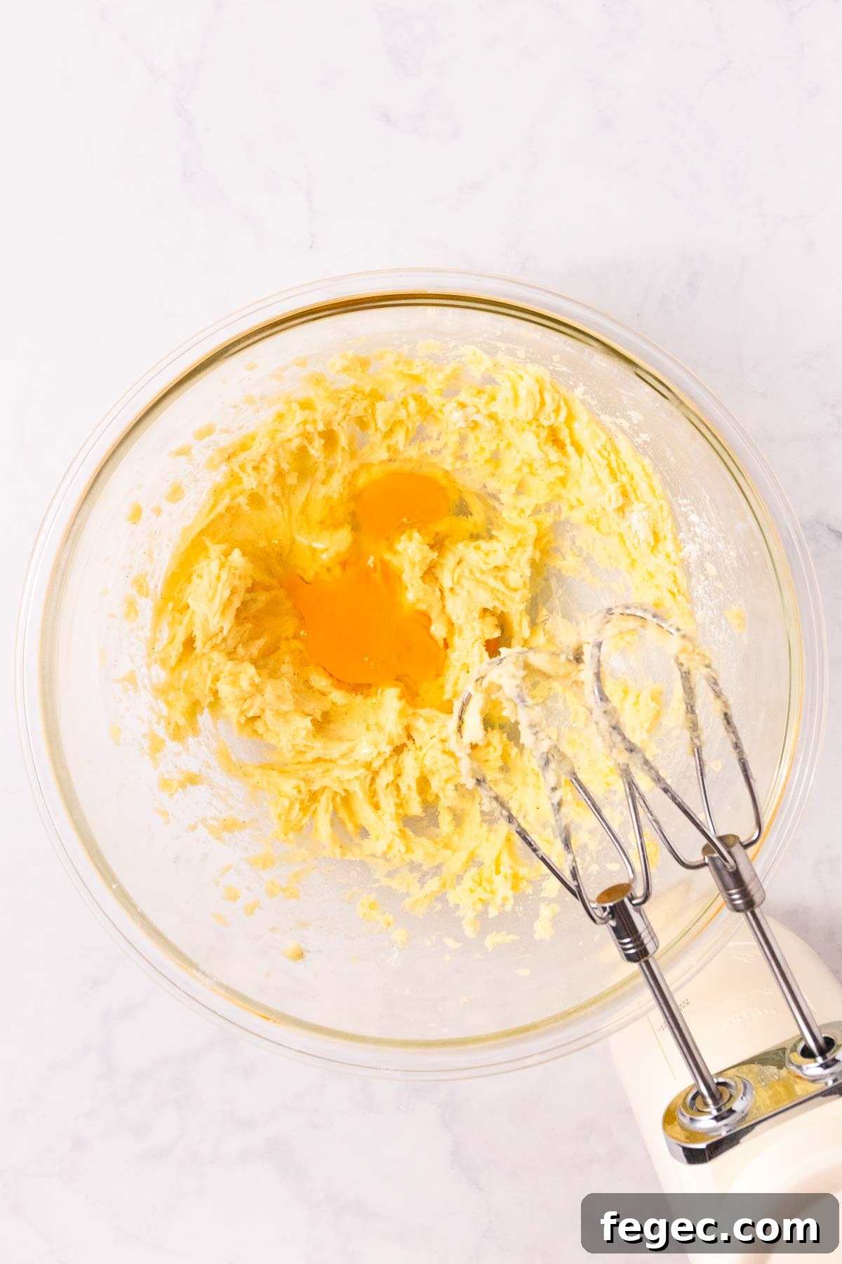 The creamed butter and sugar mixture, with an egg added, in a large glass bowl.