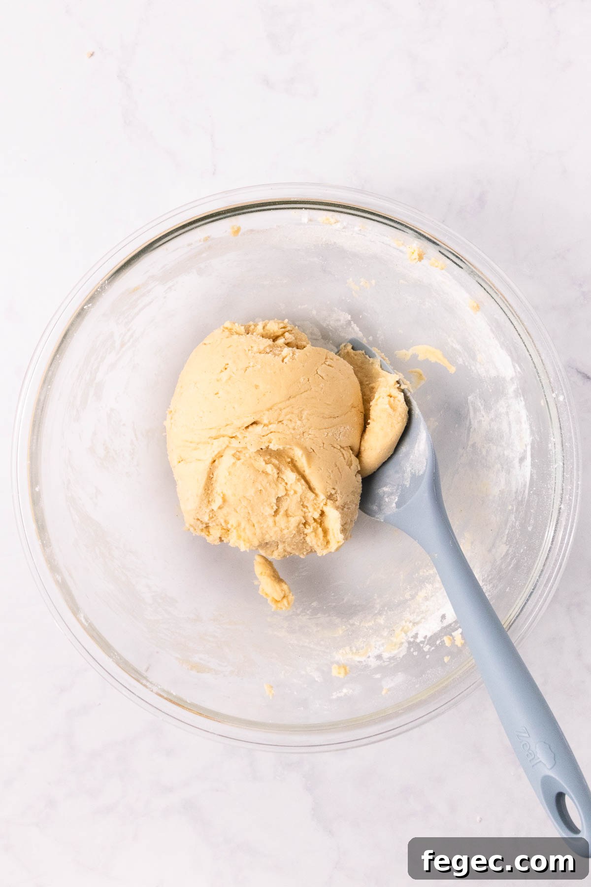 The mixed ball of dough in the glass bowl, with a large blue spatula.