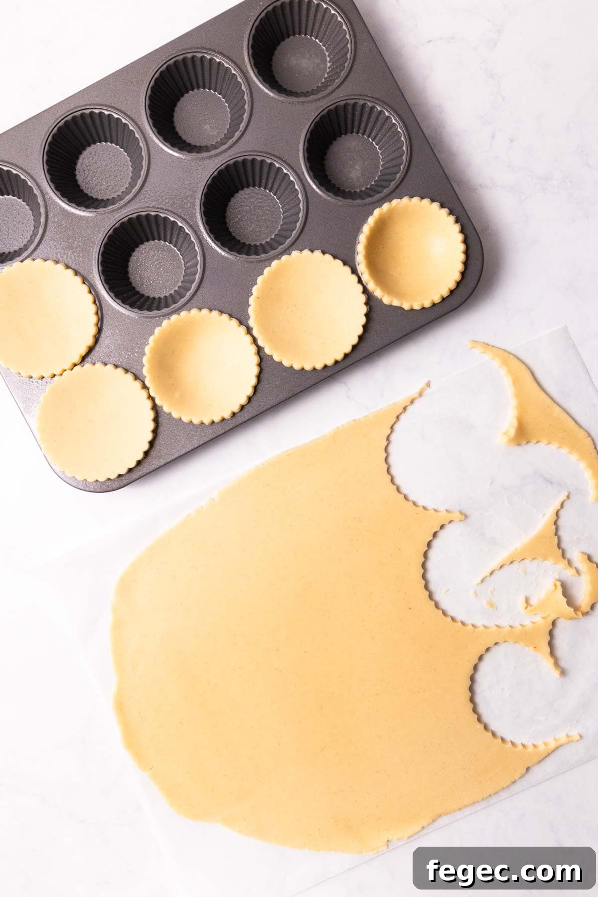 Circles of dough being cut and placed into a 12-hole fluted tart pan.