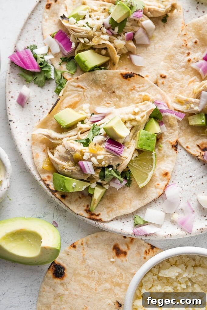 Plate full of slow cooker salsa verde chicken tacos with avocado, lime wedges, cilantro, and Cotija.