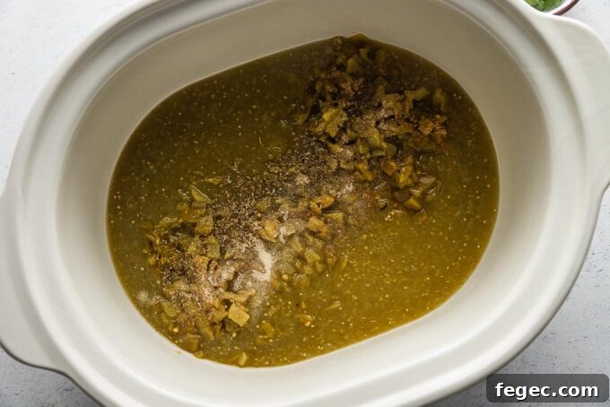 Large slow cooker bowl full of salsa verde, mild green chiles, and spices.