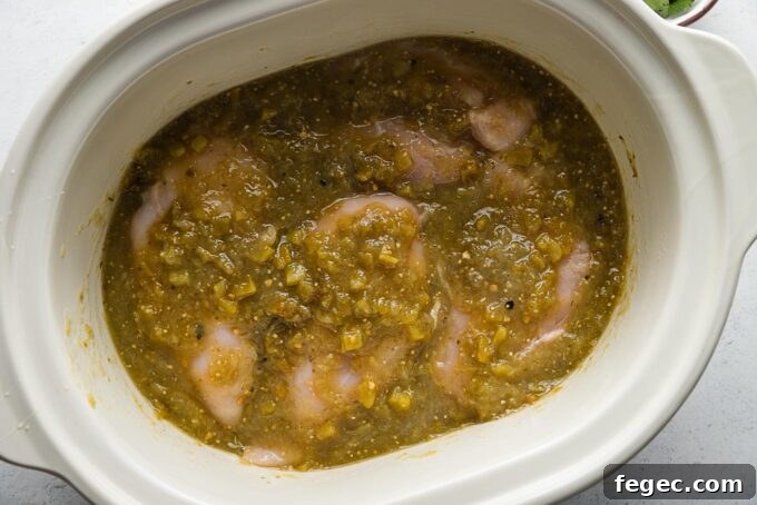 Uncooked chicken breasts added to a slow cooker and coated with a salsa verde sauce.
