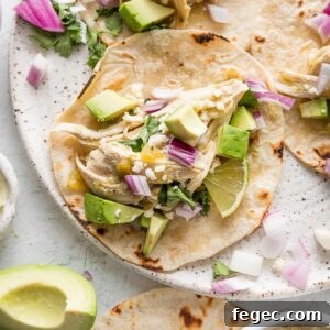 Plate full of slow cooker salsa verde chicken tacos with avocado, lime wedges, cilantro, and Cotija.