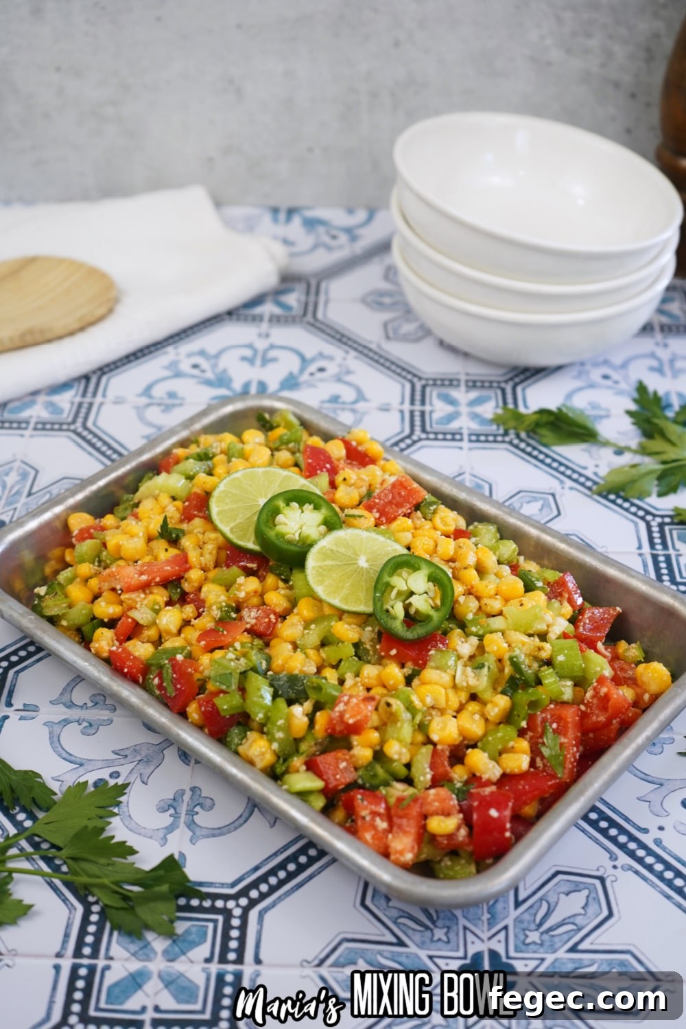 finished spicy corn salad in a metal tray with slices of limes and jalapenos on the top
