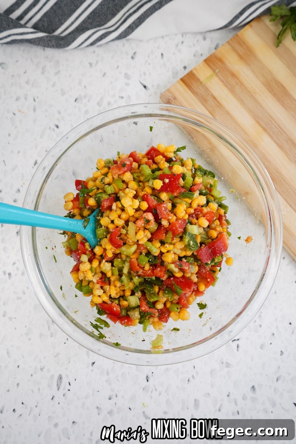 corn salad being mixed with a rubber spatula in a glass mixing bowl