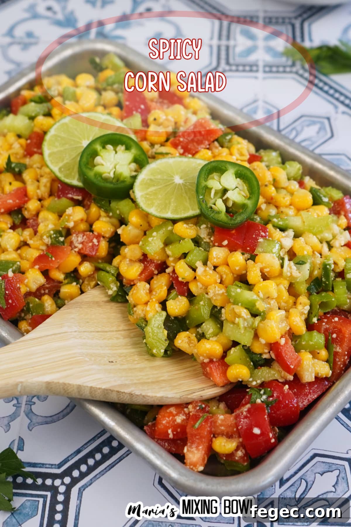 finished spicy corn salad in a metal tray with slices of limes and jalapenos on the top