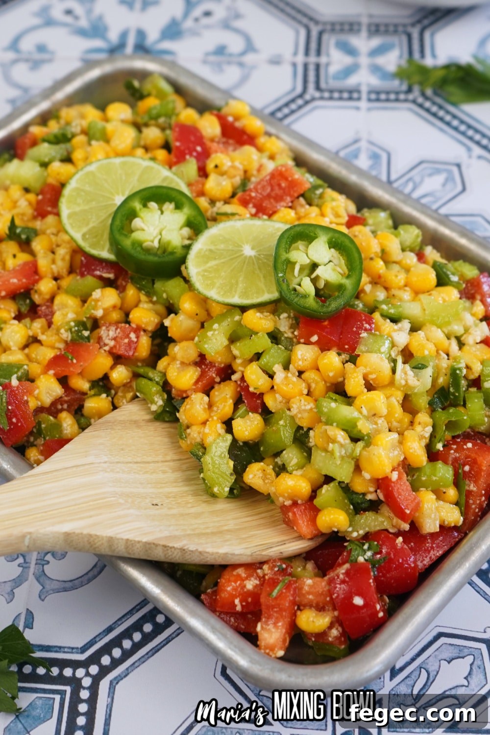 finished spicy corn salad in a metal tray with slices of limes and jalapenos on the top