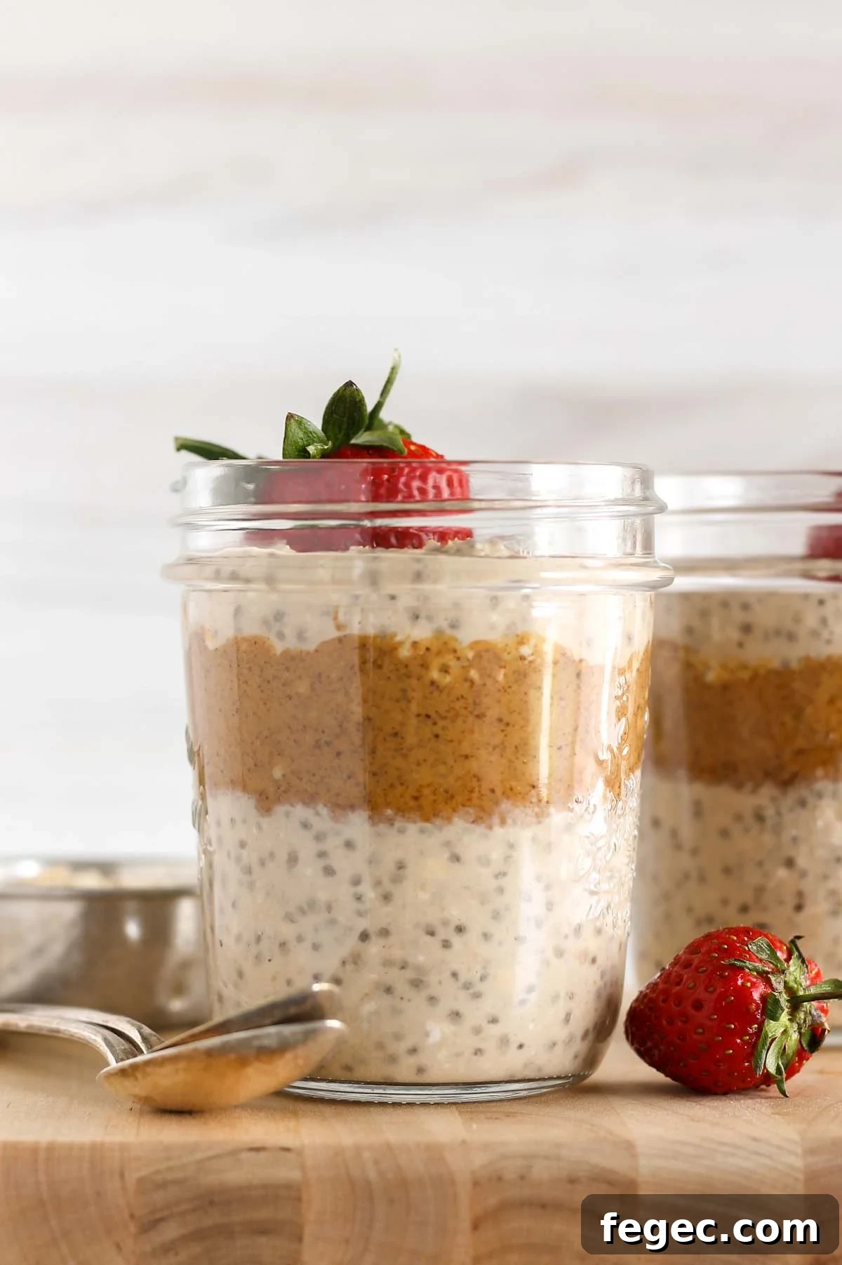 High-Protein Overnight Oats — 5-Ingredient Recipe 2 Mason jar filled with layers of overnight oats and almond butter topped with a strawberry.