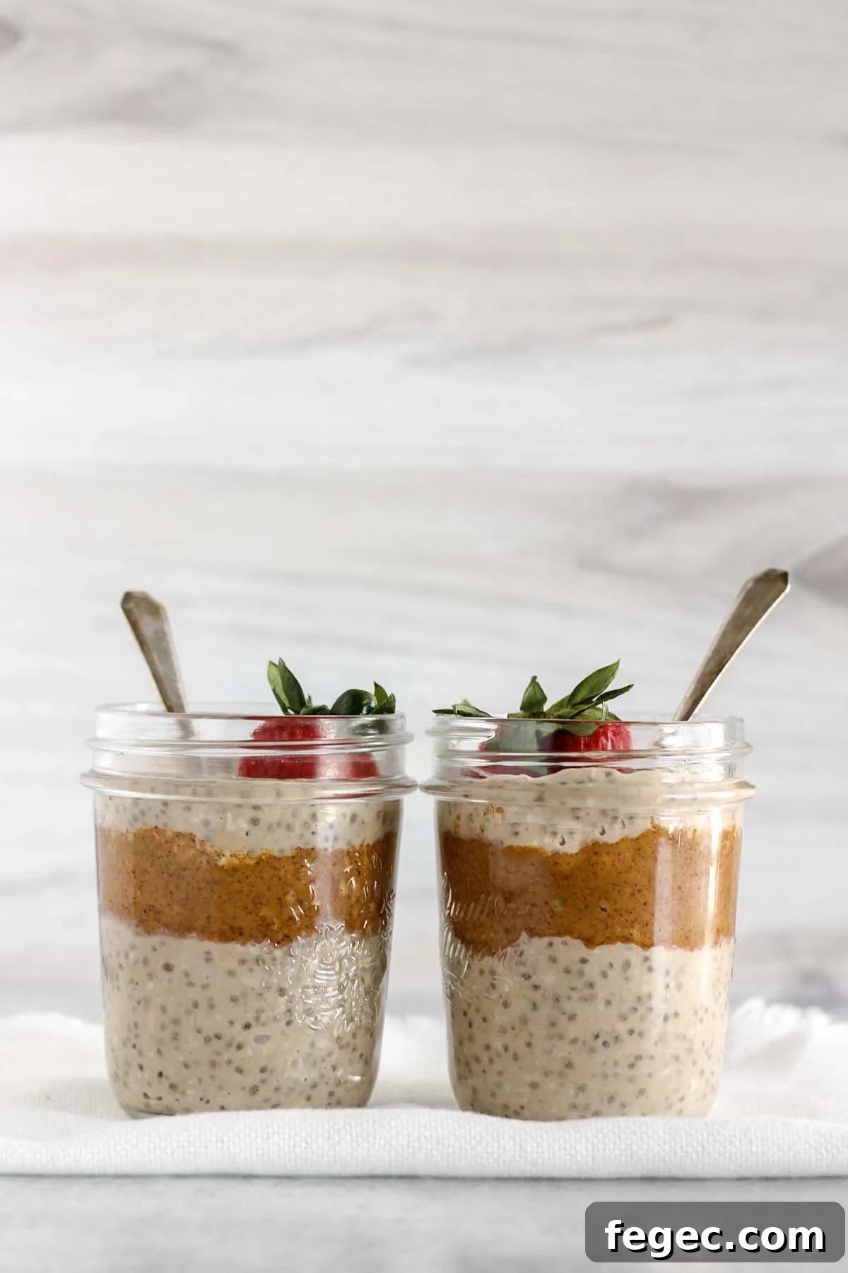 High-Protein Overnight Oats — 5-Ingredient Recipe 6 Two mason jars filled with overnight oats and almond butter topped with a strawberry.