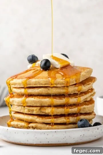 Syrup being poured over a stack of oat flour pancakes topped with blueberries.