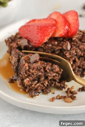 Gold fork cutting a bite off of a piece of chocolate baked oats topped with strawberries.