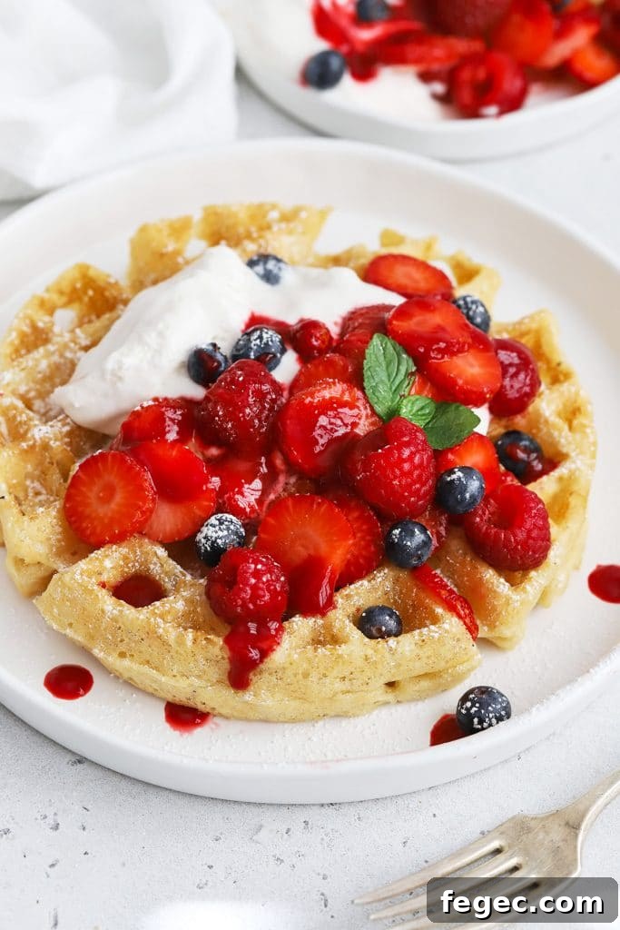 Front view of gluten-free Belgian waffles topped with berries, whipped cream, and raspberry syrup