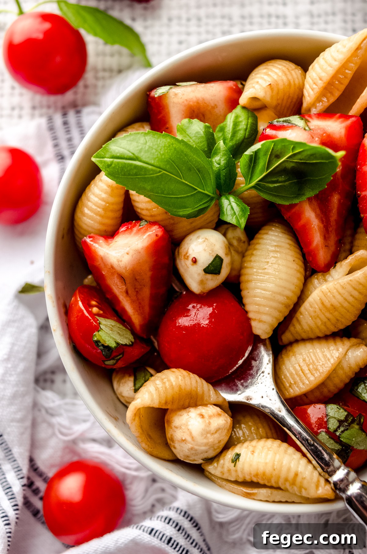 Closeup of a fork in a bowl of strawberry caprese pasta salad in a small white bowl.