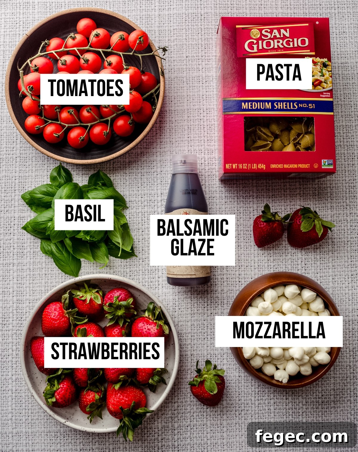 Aerial photo of ingredients for strawberry caprese pasta salad with text overlay labeling each ingredient.