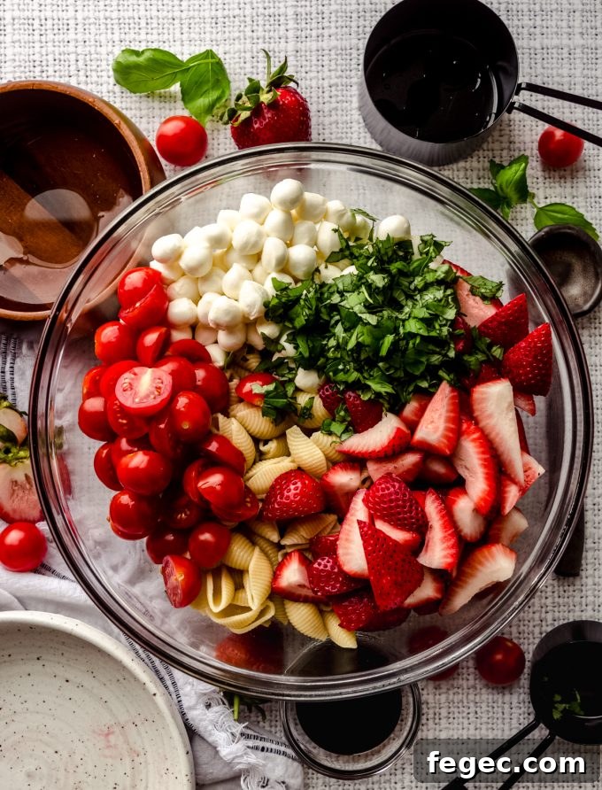 Aerial photo of a bowl of the components to make strawberry caprese pasta salad.