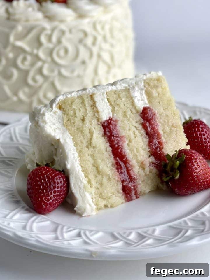 A slice of vanilla strawberry cake with the decorated vanilla cake in the background.