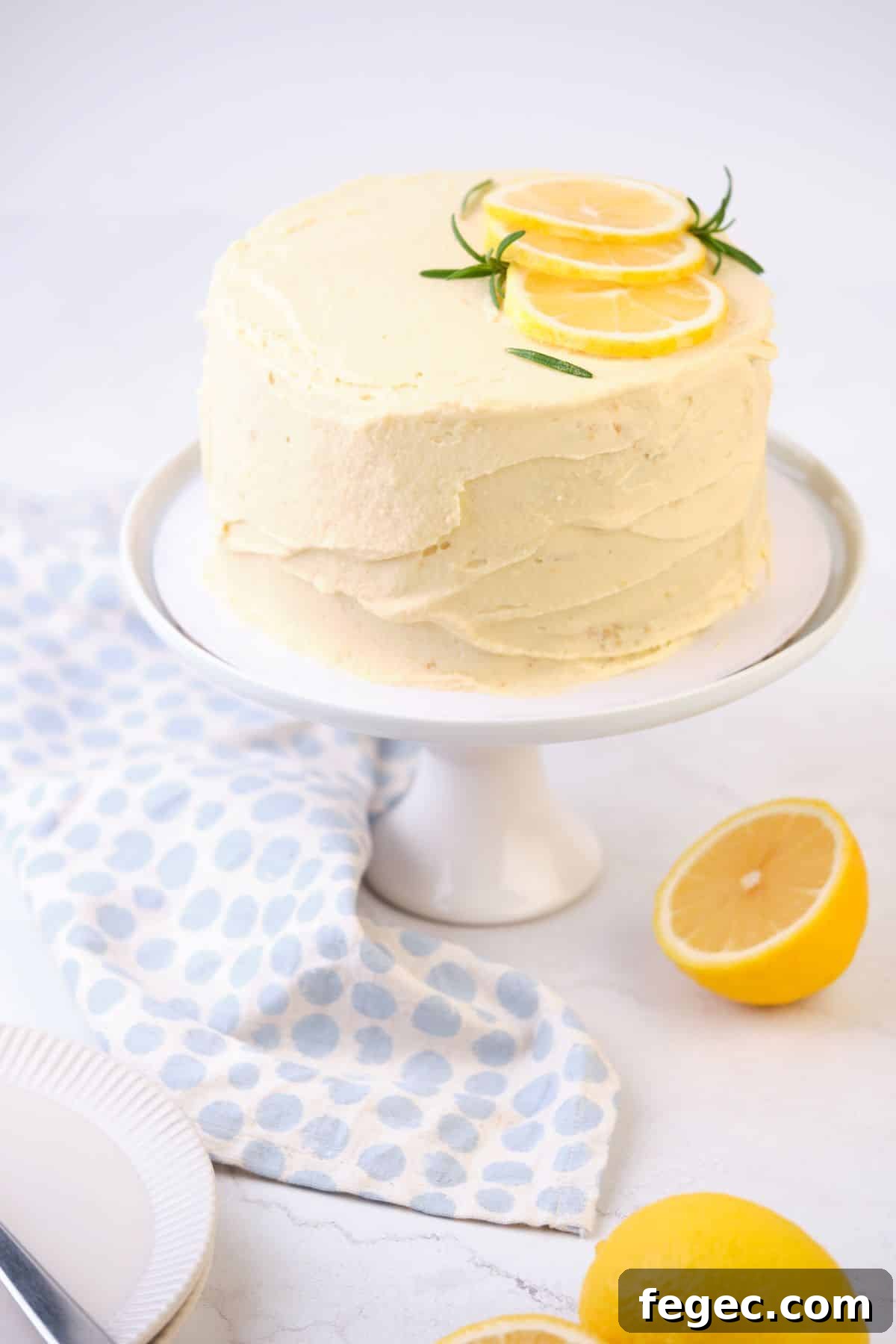 A lemon layer cake on a cake pedestal decorated with fresh lemons.
