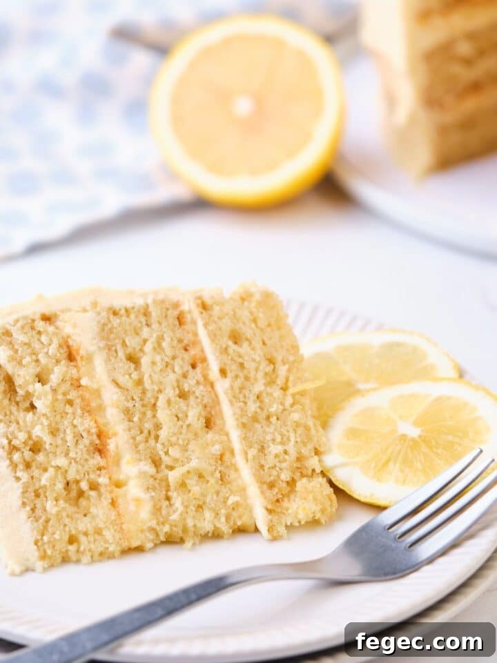 A slice of lemon curd cake on a plate with the lemon curd layer cake in the background.