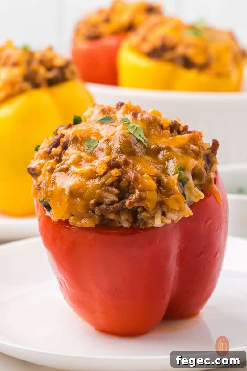 An eye-level shot of a single baked red taco stuffed pepper on a white plate, with the top of a yellow pepper visible in the blurred background.