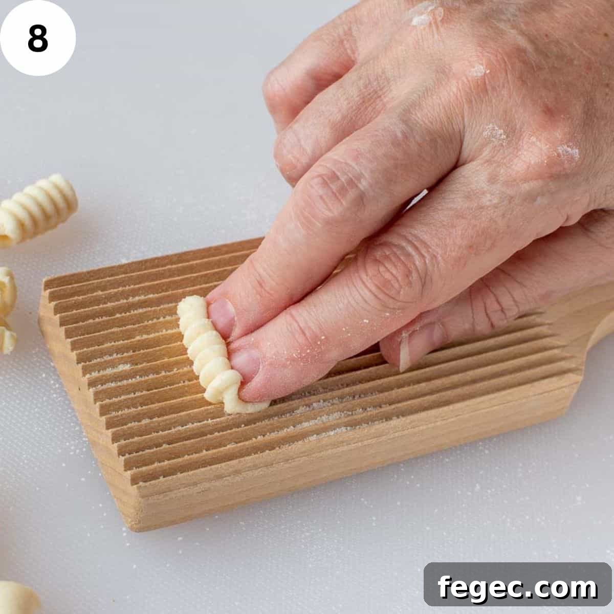 Two fingers using the a ridged board to shape pasta dough.