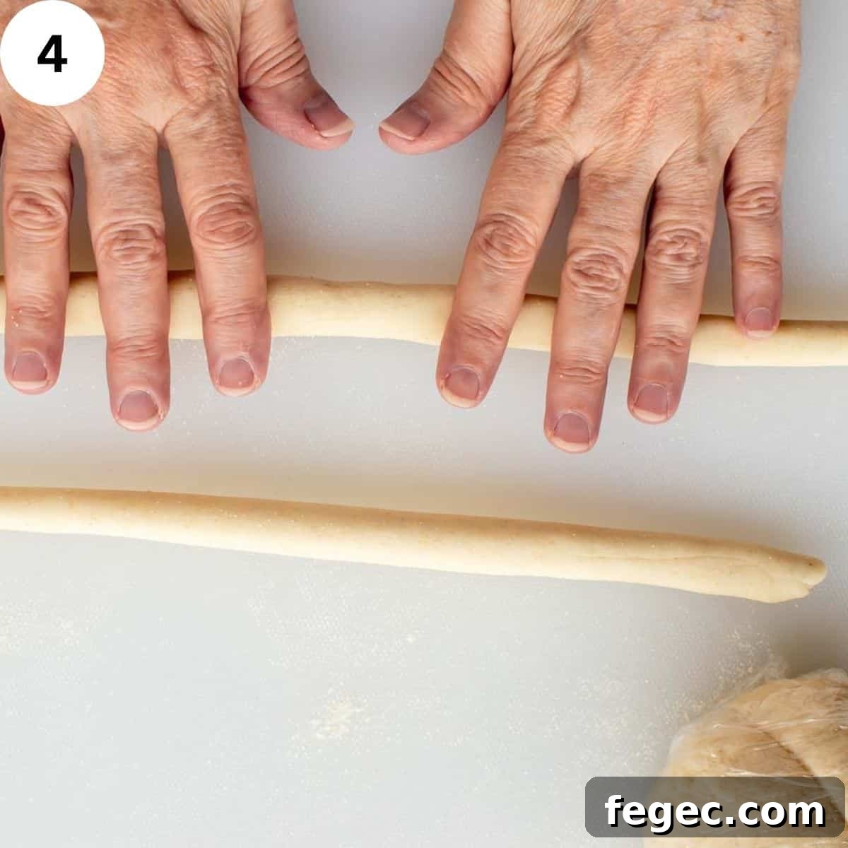Hands rolling pasta dough into long logs. 