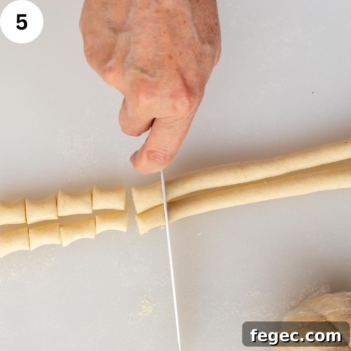 Cutting ropes of semolina pasta into short pieces.